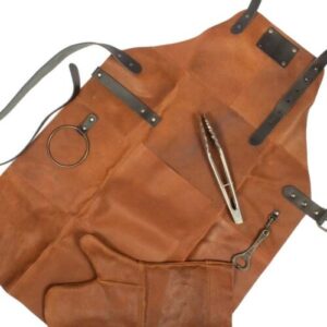 Set Asador de Gamuza de Búfalo. Deluxe set de Asador, contiene Pechera de Asador BBQ en Cuero engamuzado 100% genuino color café cognac, con cintas y rectángulo de Cuero 100% genuino color negro. Argolla, destapador y remaches de acero envejecido y bolsillo delantero grande. Contiene además largo mitón de Asador BBQ en Cuero engamuzado 100% genuino color café cognac y tenazas de Acero inoxidable.