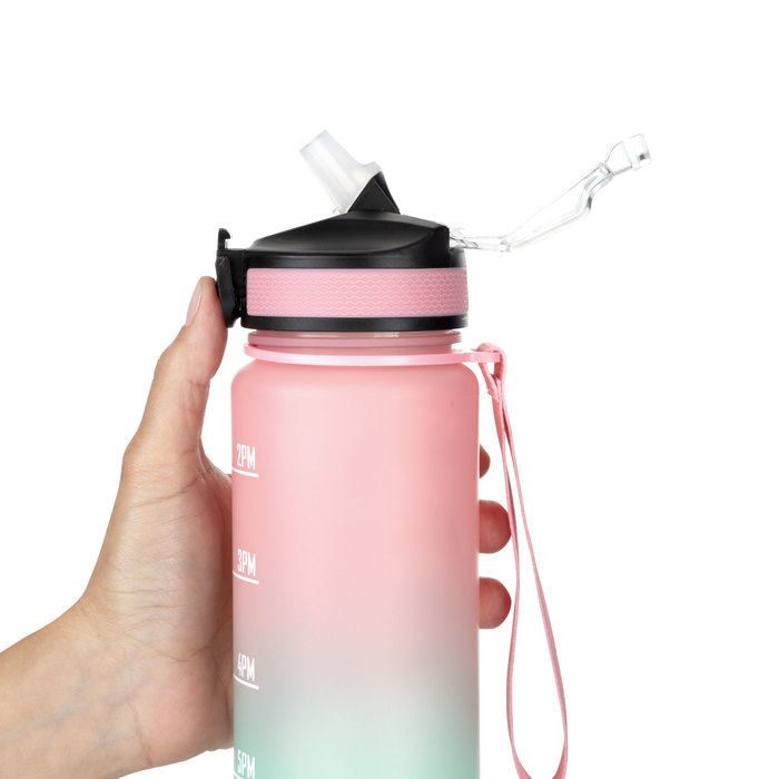 Mano sosteniendo la botella deportiva motivacional GRAF en color rosa/aguamarina con acabado traslucido, con contador de tiempo y medidor y su cinta de transporte en color rosa.