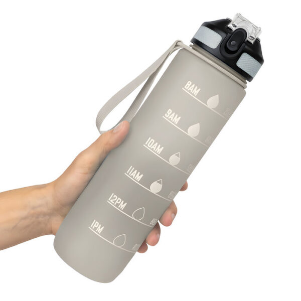 Mano sosteniendo una botella deportiva motivacional NADAL en color gris con acabado frost, con contador de tiempo, tapa con boquilla rebatible y correa