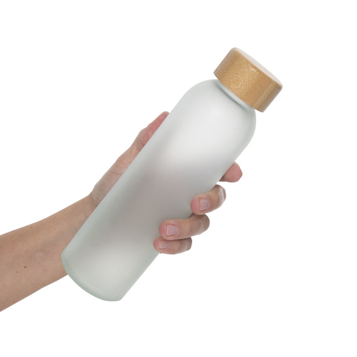 Mano sosteniendo Botella sublimable SANDER, hecha de vidrio resistente con un elegante acabado frost, con tapa de bambú